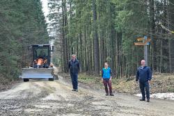 Vom Erfolg der Radweg-Instandsetzung durch die DB Netz AG überzeugten sich Nationalparkleiter Franz Leibl (links), Försterin Silvia Pflug und Bürgermeister Michael Herzog. Für die Reparaturmaßnahme wurde ein Grader (Hintergrund) eingesetzt.  (Foto: Elke Ohland/Nationalpark Bayerischer Wald)